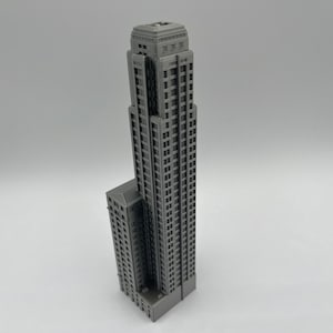 May include: A gray 3D printed model of a tall skyscraper building with a smaller building attached to the side.