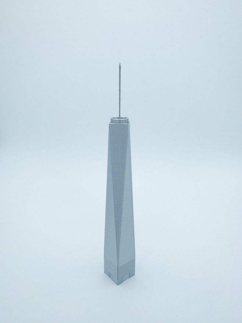 May include: A gray model of the One World Trade Center building with a pointed spire on top.