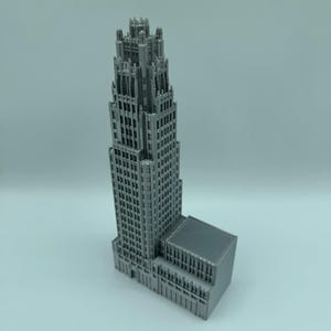 May include: A gray, 3D-printed model of a skyscraper. The building features a detailed facade with numerous windows and architectural details. The model is a miniature representation of a tall building.