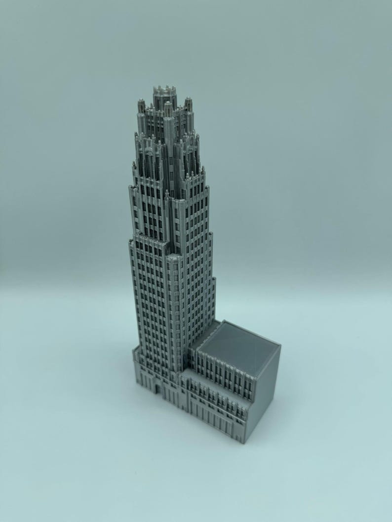 May include: A gray, 3D-printed model of a skyscraper. The building features a detailed facade with numerous windows and architectural details. The model is a miniature representation of a tall building.