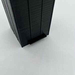May include: A black, rectangular, tall building model with a small platform at the bottom.