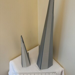May include: Two gray 3D printed models of a skyscraper. The larger model is about 11 inches tall and the smaller model is about 4 inches tall.