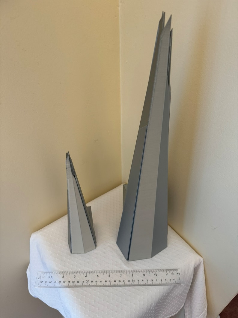 May include: Two gray 3D printed models of a skyscraper. The larger model is about 11 inches tall and the smaller model is about 4 inches tall.