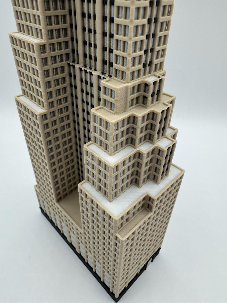 May include: A detailed 3D-printed model of a skyscraper, featuring multiple tiers and a complex architectural design. The building is primarily beige with white accents, showcasing a realistic representation of a modern high-rise structure. The model sits on a black base.