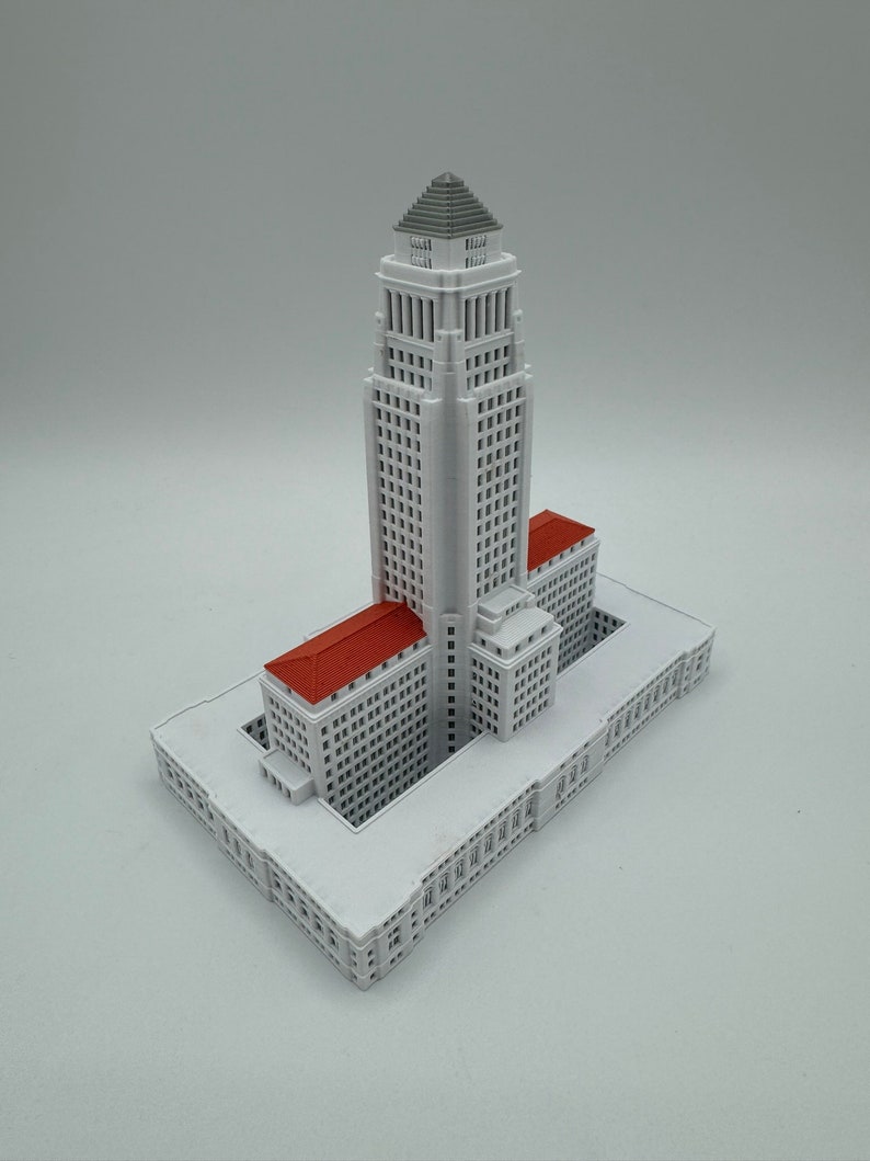 May include: A white 3D printed model of the Los Angeles City Hall building. The model is detailed and includes the iconic tower and surrounding buildings.