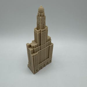 May include: A detailed miniature model of a tall, beige building with a domed roof and many windows. The building has a clock face on the front.