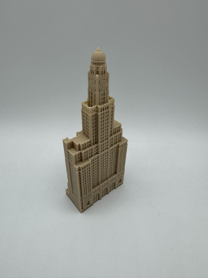 May include: A detailed miniature model of a tall, beige building with a domed roof and many windows. The building has a clock face on the front.