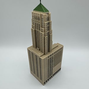 May include: A beige model of a skyscraper with a green roof and a small spire. The building has many windows and architectural details, and it sits on a rectangular base. The model is likely a replica of a famous building.