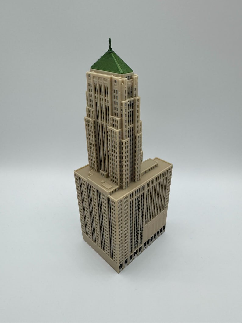 May include: A beige model of a skyscraper with a green roof and a small spire. The building has many windows and architectural details, and it sits on a rectangular base. The model is likely a replica of a famous building.