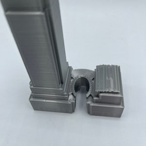 May include: A gray 3D printed model of a skyscraper with a detailed facade and a base that is separate from the tower.
