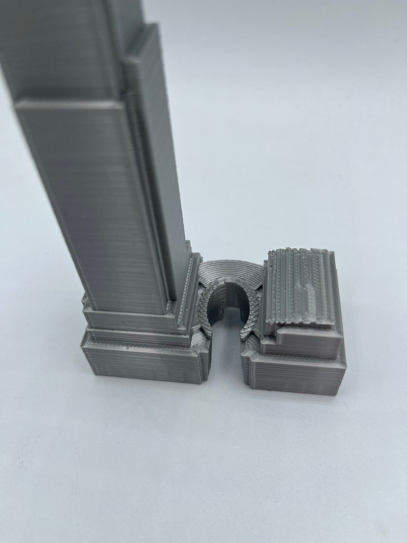 May include: A gray 3D printed model of a skyscraper with a detailed facade and a base that is separate from the tower.