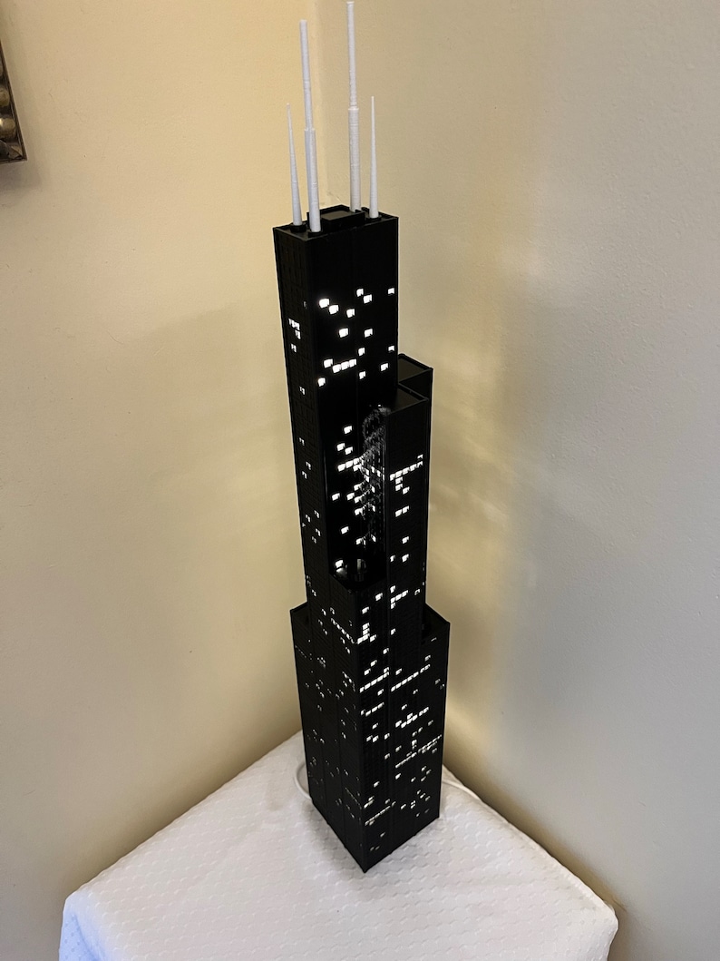 May include: A black model of the Willis Tower, formerly known as the Sears Tower, with white antenna details. The model is lit up with white lights, creating a realistic nighttime cityscape effect.