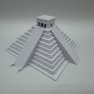 May include: A light gray scale model of a stepped pyramid featuring four sides with tiered levels and a central staircase leading to a flat-topped temple structure at the summit. The architectural replica displays geometric precision and smooth surfaces.