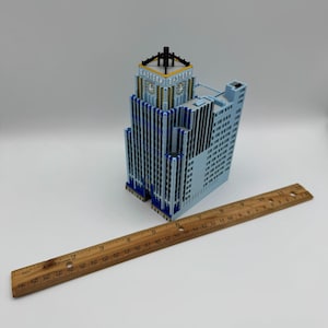 May include: A light blue architectural model of a skyscraper with blue and gold accents. The model has the word "EASTERN" on the top. A wooden ruler, 30 inches long, is placed next to the building.