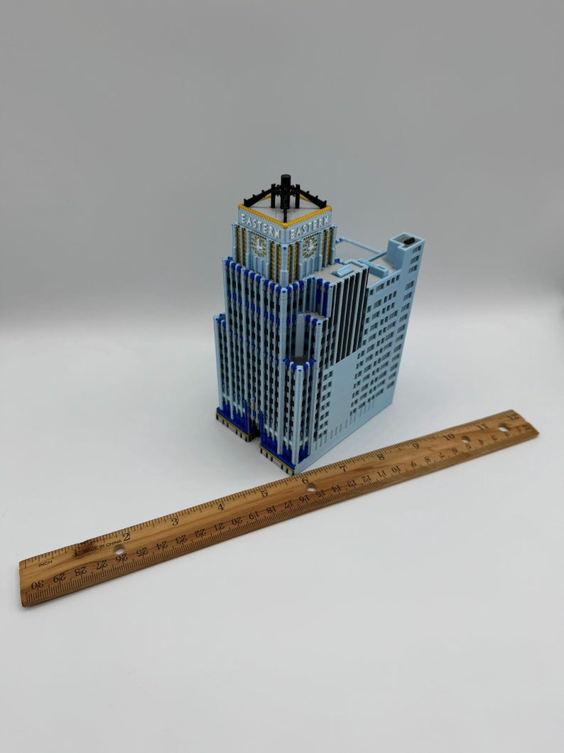 May include: A light blue architectural model of a skyscraper with blue and gold accents. The model has the word "EASTERN" on the top. A wooden ruler, 30 inches long, is placed next to the building.