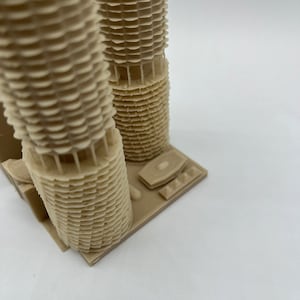 May include: A beige 3D printed model of a skyscraper with a detailed facade. The model is on a small base.