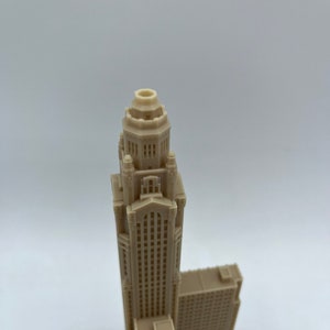 May include: A beige 3D printed model of a tall skyscraper with a decorative top and many windows.