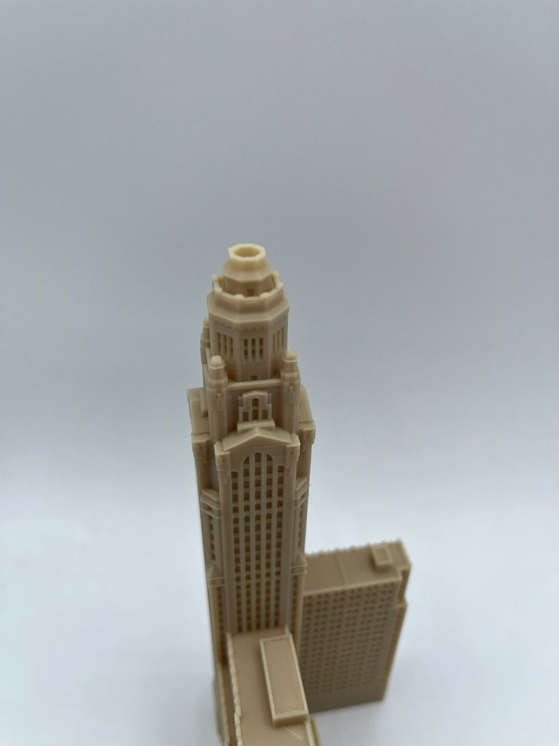 May include: A beige 3D printed model of a tall skyscraper with a decorative top and many windows.