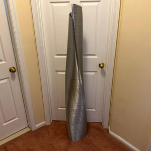 May include: A silver metal floor lamp with a unique twisted design. The lamp is standing in a hallway with two white doors.