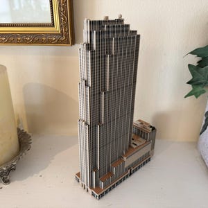 Puede incluir: Modelo detallado de un rascacielos, con un dise&ntilde;o escalonado y l&iacute;neas verticales en tonos grises y marrones. El modelo arquitect&oacute;nico se alza sobre una superficie blanca, mostrando su intrincada fachada. Art&iacute;culo decorativo.