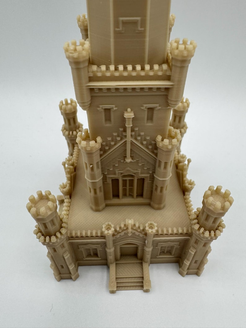 May include: A beige miniature castle model with multiple turrets and architectural details. The model features a central tower and several smaller towers, with detailed windows and crenellations. The overall design is intricate and symmetrical, showcasing a detailed miniature building.