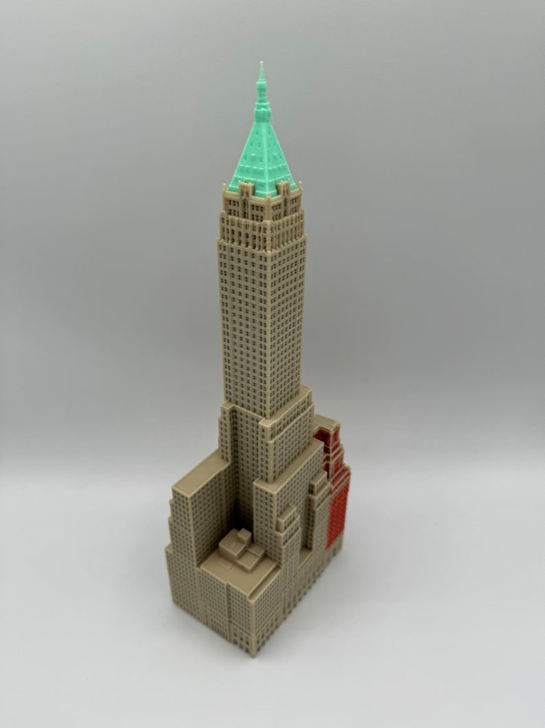 May include: A miniature model of a tall, brown building with a green roof and a red accent. The building has many windows and a detailed facade.