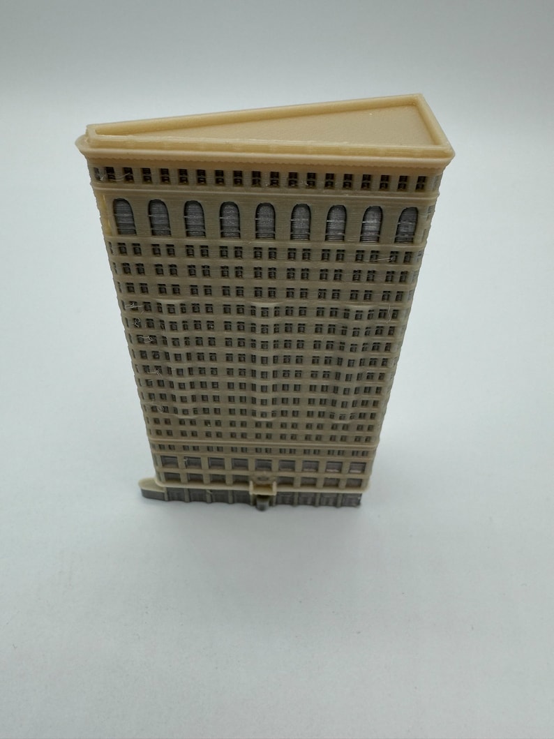May include: A beige miniature model of a skyscraper with a triangular roof and many windows. The model is made of plastic and has a detailed facade.