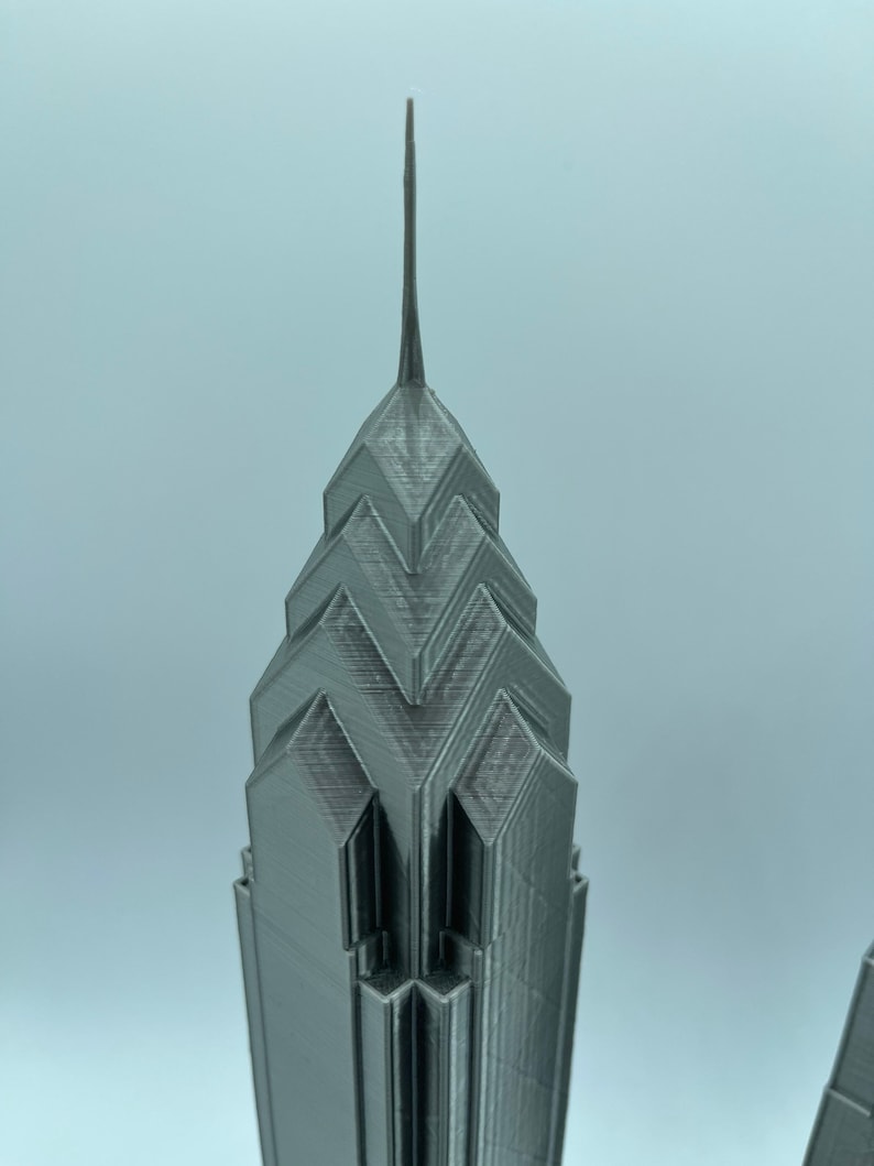 May include: A 3D printed model of a skyscraper with a pointed top and a geometric design. The model is made of a gray plastic material.