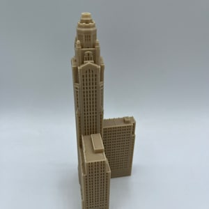 May include: A beige 3D printed model of a tall skyscraper with a smaller building attached to the side.