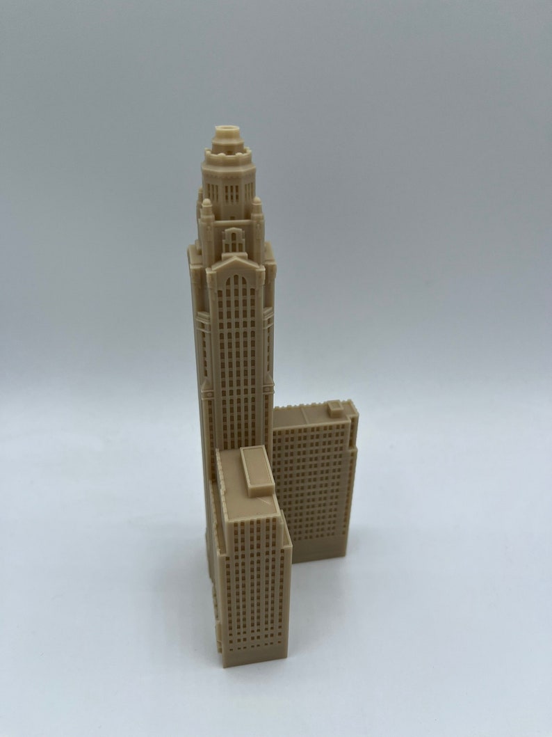 May include: A beige 3D printed model of a tall skyscraper with a smaller building attached to the side.