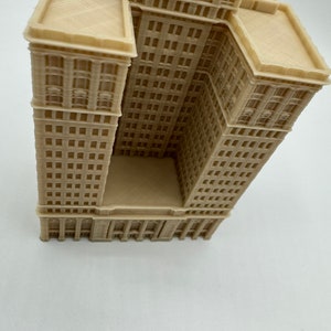 May include: A beige 3D printed model of a tall building with a flat roof and many windows. The building is angled to show the side and front of the structure.