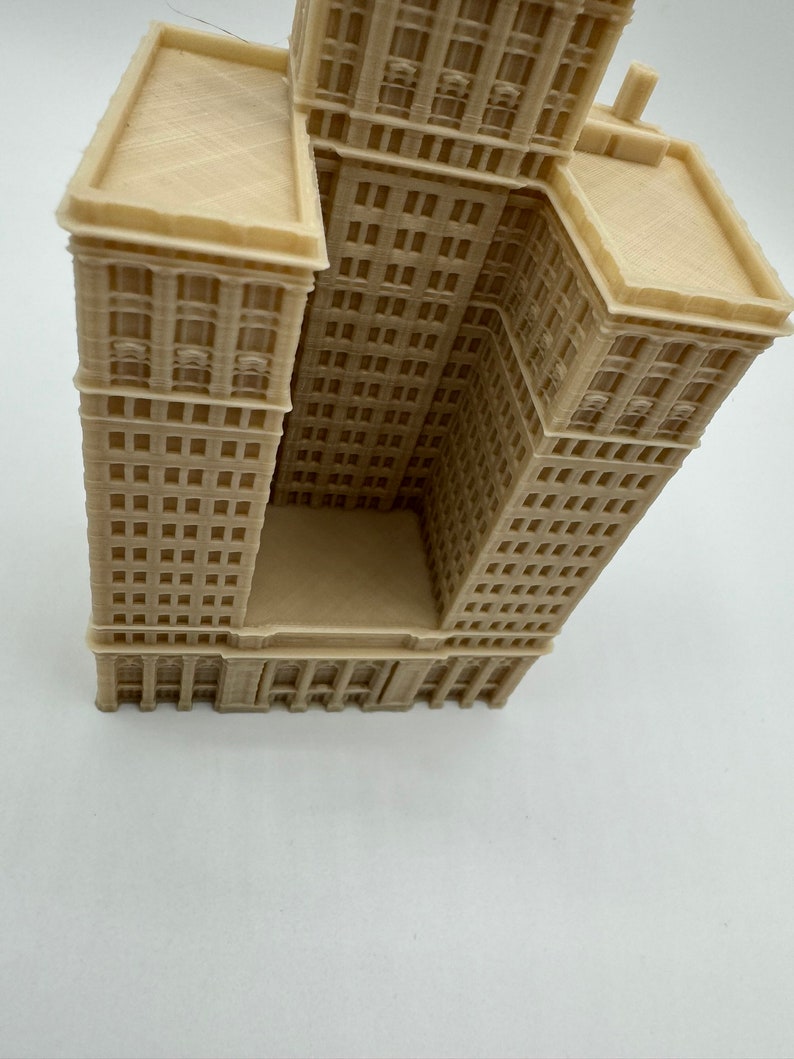 May include: A beige 3D printed model of a tall building with a flat roof and many windows. The building is angled to show the side and front of the structure.