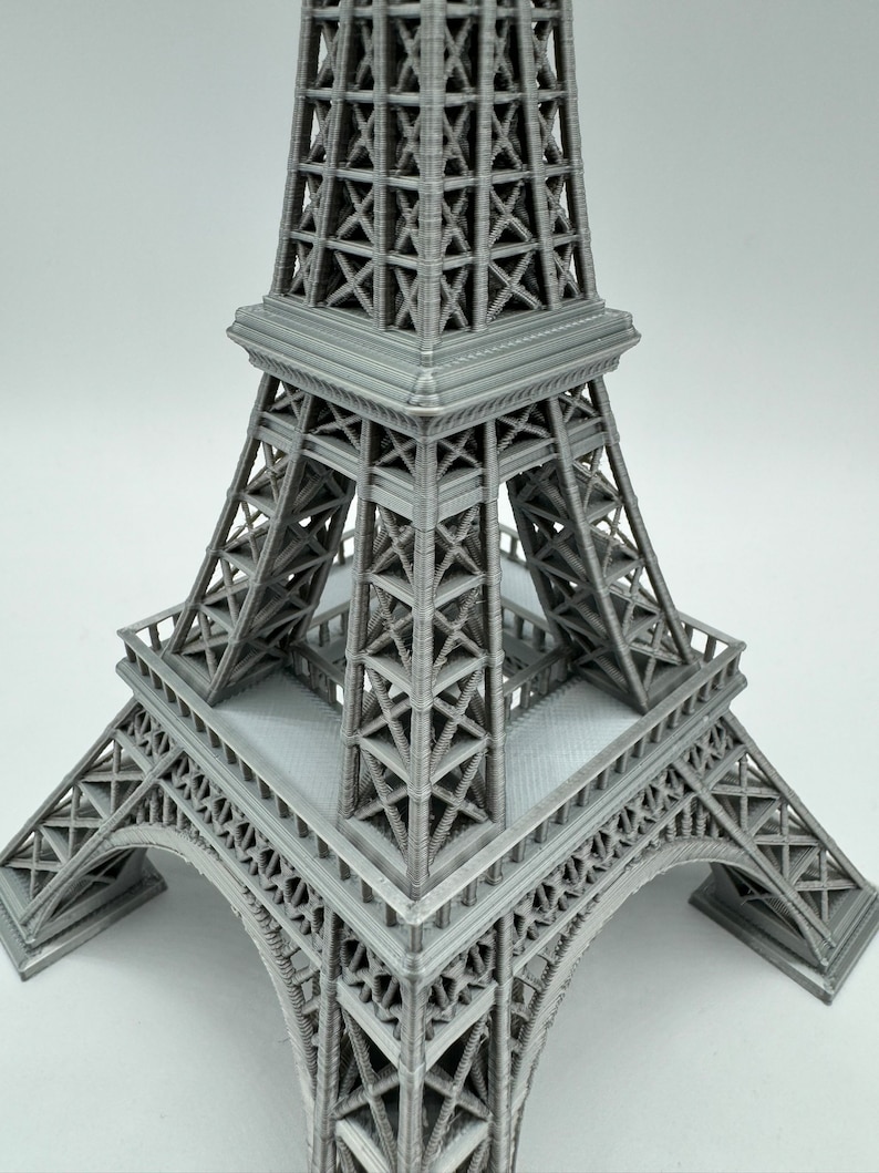 May include: A gray 3D printed model of the Eiffel Tower. The model is detailed and shows the intricate structure of the tower.