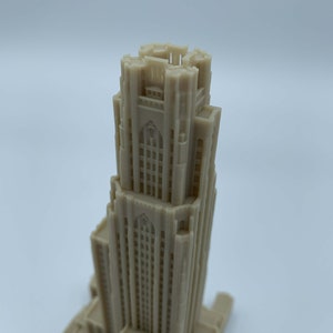 May include: A detailed 3D printed model of a tall building with a pointed roof and many windows. The model is made of a light beige plastic.
