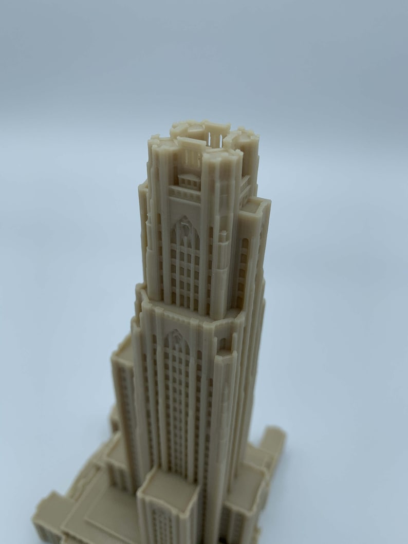 May include: A detailed 3D printed model of a tall building with a pointed roof and many windows. The model is made of a light beige plastic.