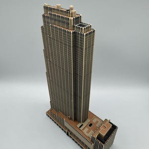 Puede incluir: Maqueta arquitect&oacute;nica detallada de un rascacielos. El modelo presenta una torre alta y rectangular con l&iacute;neas verticales y una parte superior de varios niveles. La base del edificio tiene un dise&ntilde;o detallado. La paleta de colores es principalmente beige y marr&oacute;n.