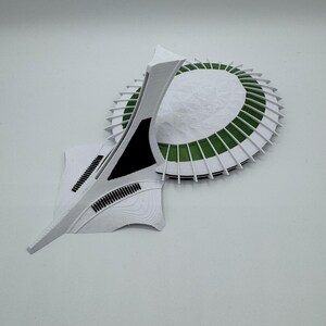 Puede incluir: Maqueta arquitect&oacute;nica abstracta en blanco y verde. El dise&ntilde;o incluye una base circular con detalles verdes y una estructura alta y angular. Los detalles en negro y la superficie texturizada completan la est&eacute;tica moderna.