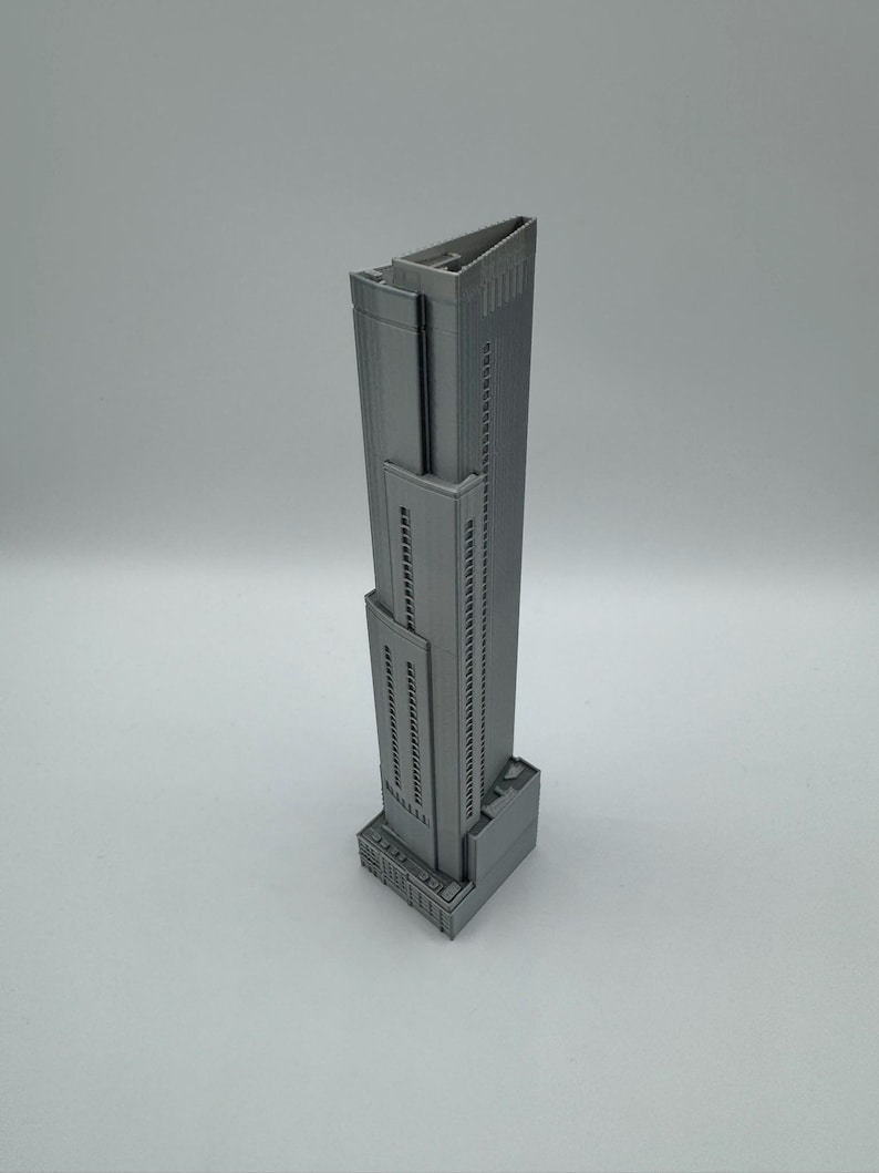 May include: A gray, 3D-printed model of a skyscraper. The building has a rectangular base, a tall, slender main structure with many windows, and a flat roof. The model is a solid, monochromatic gray.