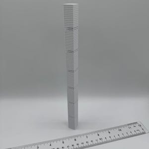 May include: A grey, miniature skyscraper model with a detailed facade. A ruler is placed in front of the building. The model appears to be approximately 25 cm tall.
