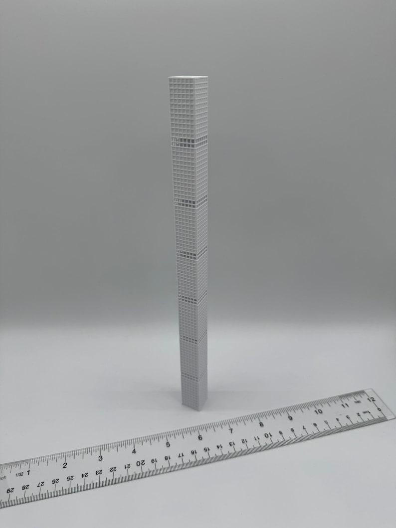 May include: A grey, miniature skyscraper model with a detailed facade. A ruler is placed in front of the building. The model appears to be approximately 25 cm tall.