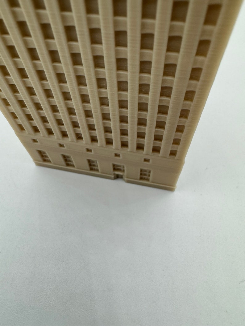 Pu&ograve; includere: Un modello di edificio alto di colore beige stampato in 3D con un motivo a griglia sulla facciata e una fila di finestre alla base.