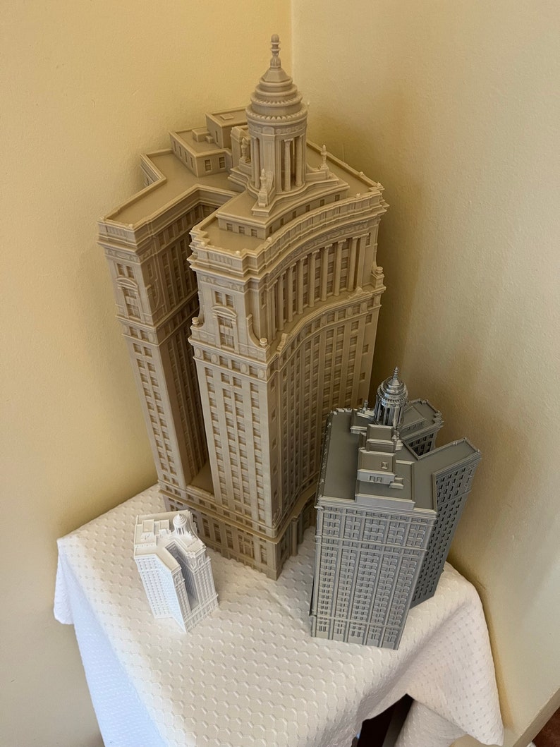 Op de afbeelding: Drie miniatuurgebouwenmodellen, een beige met een koepel, een grijs met een koepel en een wit met een koepel, op een wit tafelkleed.