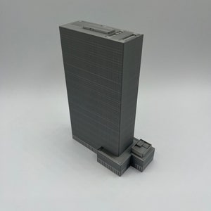 May include: A gray 3D printed model of a skyscraper with a flat roof and a small rectangular building at the base.
