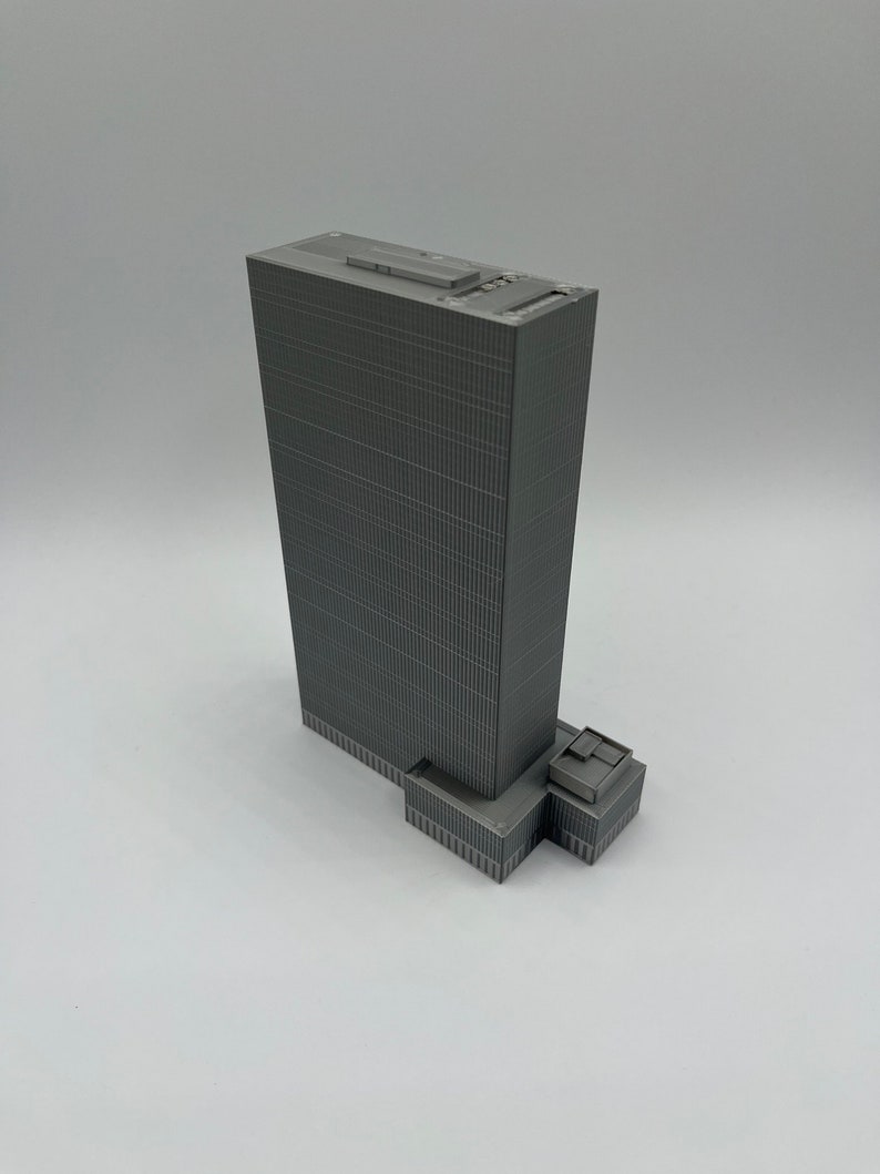 May include: A gray 3D printed model of a skyscraper with a flat roof and a small rectangular building at the base.