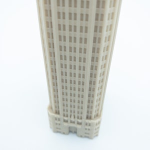May include: A beige miniature model of a tall building with many windows. The building has a simple design with a flat roof and a few decorative details.