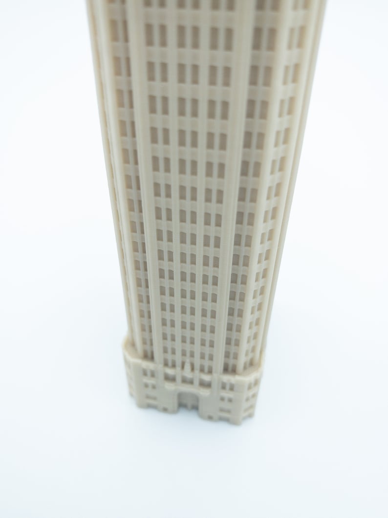 May include: A beige miniature model of a tall building with many windows. The building has a simple design with a flat roof and a few decorative details.