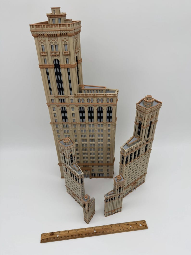 May include: Four beige miniature building models with architectural details, including windows and decorative elements. A wooden ruler is placed near the buildings. The buildings vary in size, with the tallest one being the largest.