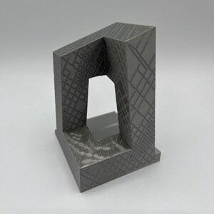 Peut inclure: Une sculpture en gris imprim&eacute;e en 3D avec un design g&eacute;om&eacute;trique. La sculpture a une base carr&eacute;e et une ouverture rectangulaire au centre.
