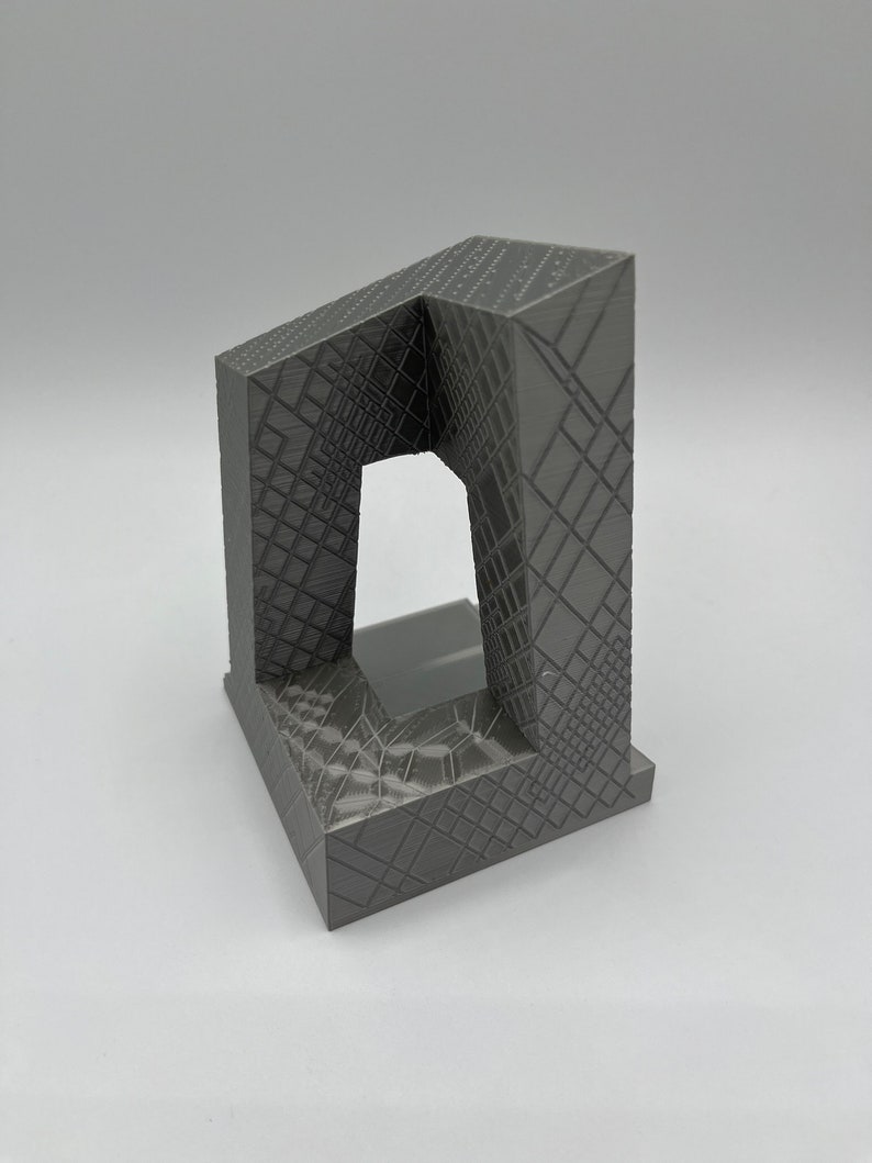 Peut inclure: Une sculpture en gris imprim&eacute;e en 3D avec un design g&eacute;om&eacute;trique. La sculpture a une base carr&eacute;e et une ouverture rectangulaire au centre.