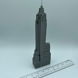 K&ouml;nnte beinhalten: Ein graues Miniaturmodell des Empire State Building mit detaillierter Fassade und Spitze. Ein Lineal liegt neben dem Modell und zeigt die Ma&szlig;e in Zentimetern an. Das Modell ist eine detaillierte Darstellung des ikonischen Wolkenkratzers.